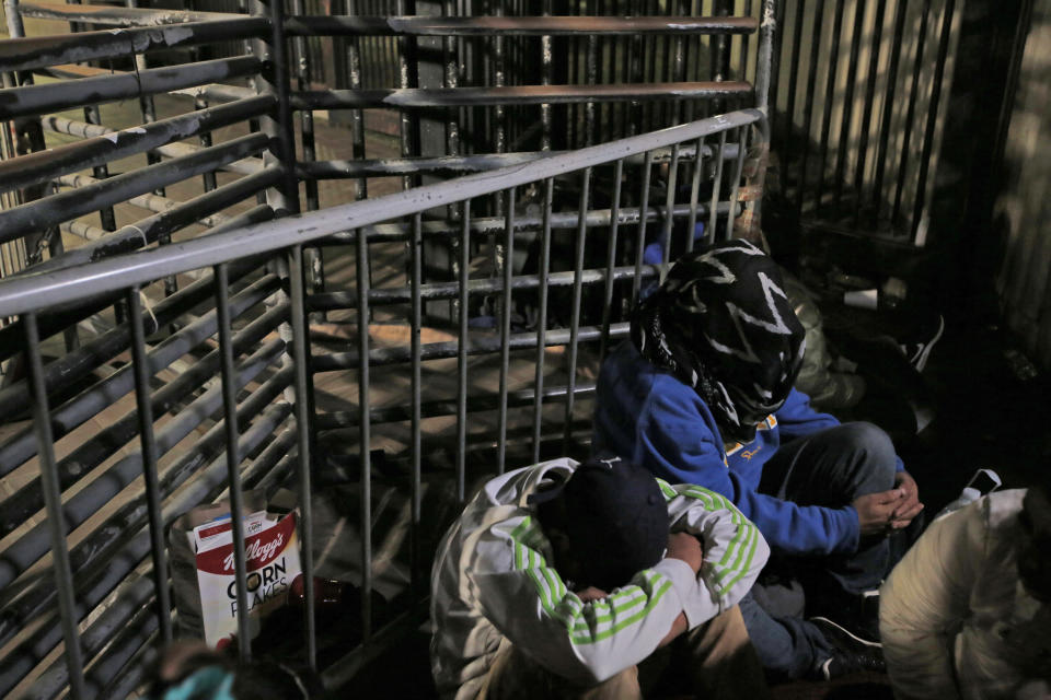 Honduran asylum seekers cover his faces surrounded by activists for migrant rights on U.S. soil at San Diego's Otay Mesa port of entry, seen from Tijuana, Mexico, Monday, Dec. 17, 2018. (AP Photo/Moises Castillo)