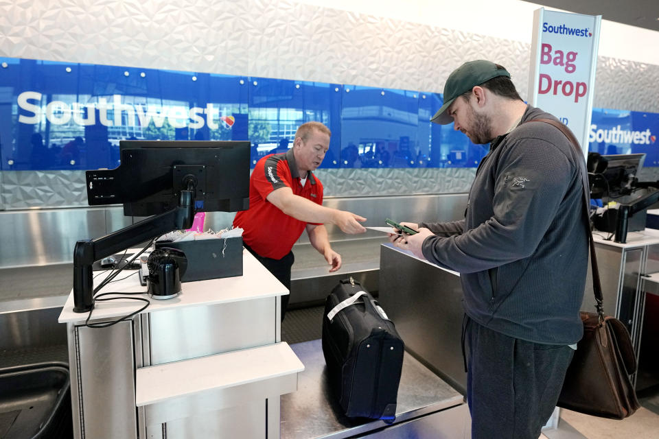 Chris Odom, right, checks his bags with a customer service representative at the Southwest ticketing gate at Love Field airport, Friday, May 19, 2023, in Dallas. The unofficial start of the summer travel season is here, with airlines hoping to avoid the chaos of last year and travelers scrounging for ways to save a few bucks on pricey airfares and hotel rooms. (AP Photo/Tony Gutierrez)