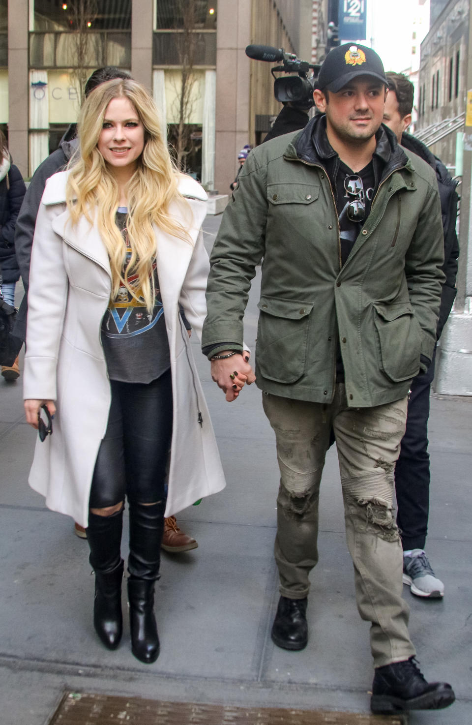 Two individuals walking hand in hand, one in a white coat and boots, the other in a green jacket and cap