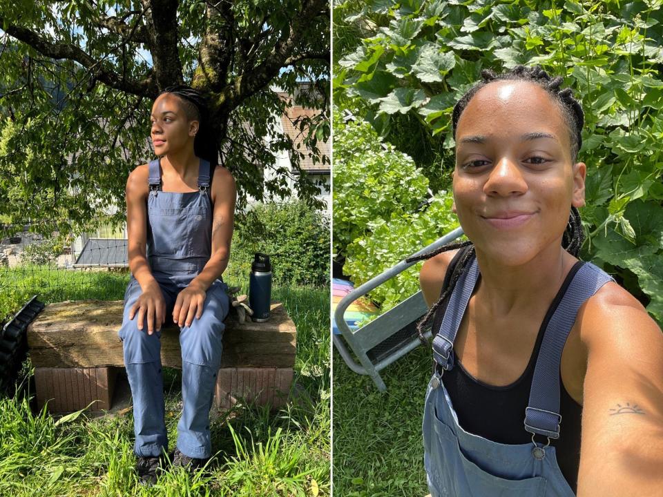 A woman wearing a black tank top and blue overalls in a garden.