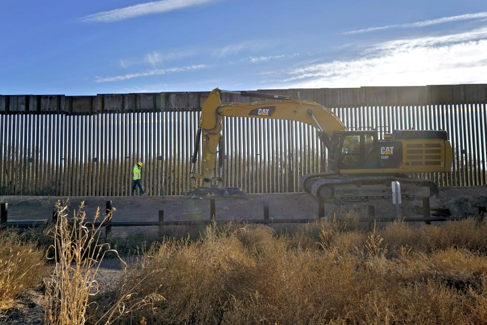 The old border fence, below grade, which allowed animal migration into Mexico, remains in place as a construction worker walks along a section of new border wall in San Bernardino National Wildlife Refuge, Tuesday, Dec. 8, 2020, in Douglas, Ariz. Construction of the border wall, mostly in government owned wildlife refuges and Indigenous territory, has led to environmental damage and the scarring of unique desert and mountain landscapes that conservationists fear could be irreversible. (AP Photo/Matt York)