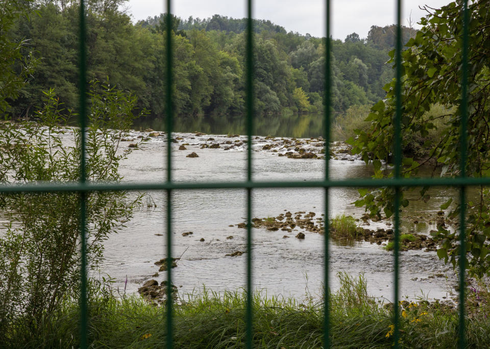 In this photo taken Friday, Aug. 23, the Kupa river on the Slovenia-Croatia border is seen through the border fence in the village of Preloka, Slovenia. Police in Croatia say a migrant has died after a van carrying 12 of them plunged into a river near the border with Slovenia, early Sunday. Slovenia started erecting additional fences on its southern border with Croatia after a considerable increase in the number of migrants trying to illegally cross between the two European Union-member states. (AP Photo/Darko Bandic)