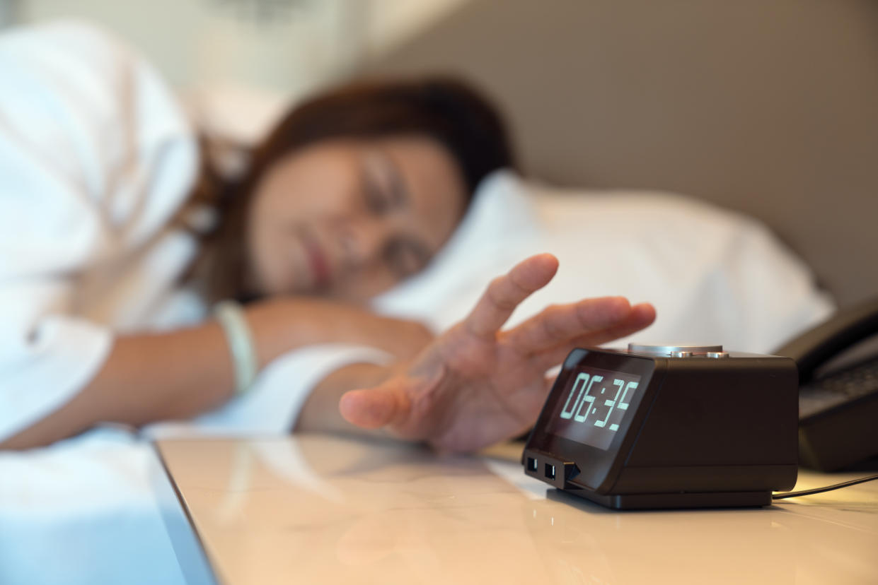 Woman sleeping in bed and reaching for alarm clock snooze button.