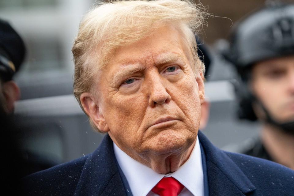 Donald Trump wearing a suit with a tie, looking serious outdoors