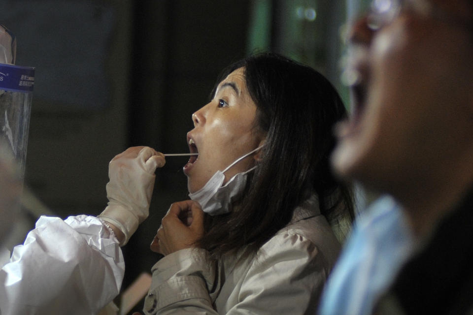 A medical staff takes a swab from a woman as residents receive the COVID-19 test near the residential area in Qingdao in east China's Shandong province on Tuesday, Oct. 13, 2020. A hospital president and the director of the health commission in the northern Chinese city of Qingdao have been fired after China's latest coronavirus outbreak, authorities said Thursday, Oct. 15, 2020. (Chinatopix via AP)