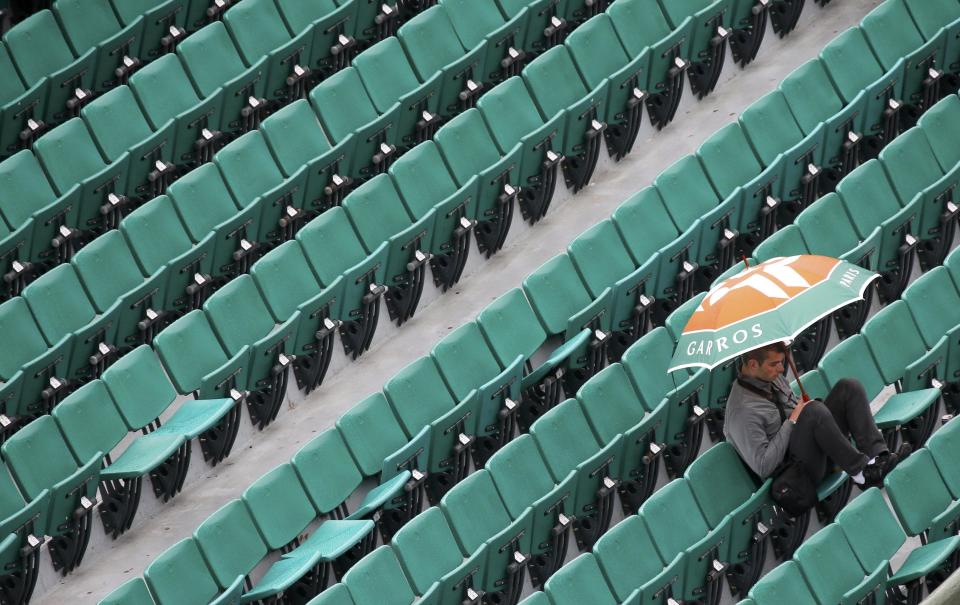 A spectator protects himself from rain during a men's singles match between Novak Djokovic of Serbia and Joao Sousa of Portugal at the French Open tennis tournament at the Roland Garros stadium in Paris May 26, 2014. REUTERS/Gonzalo Fuentes (FRANCE - Tags: SPORT TENNIS)