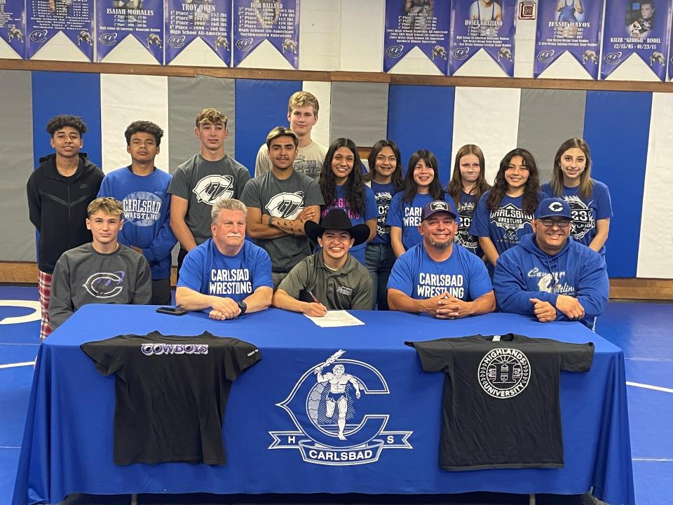 Surrounded by his teammates and coaches Carlsbad High School's Marcus Najera signs a national letter of intent to wrestle at New Mexico Highlands University in Las Vegas later this year.