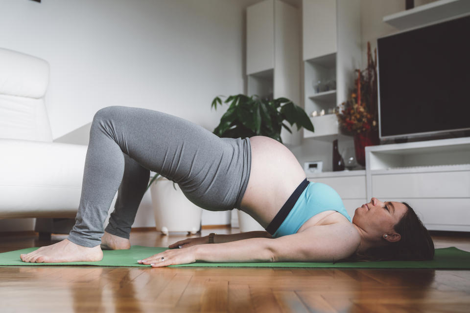 A pregnant woman performs a bridge pose exercise move whilst lying on an exercise mat