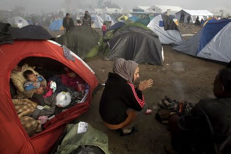 A migrant warms herself by the fire in a makeshift camp at the Greek-Macedonian border,near the Greek village of Idomeni, March 4, 2016. REUTERS/Alexandros Avramidis