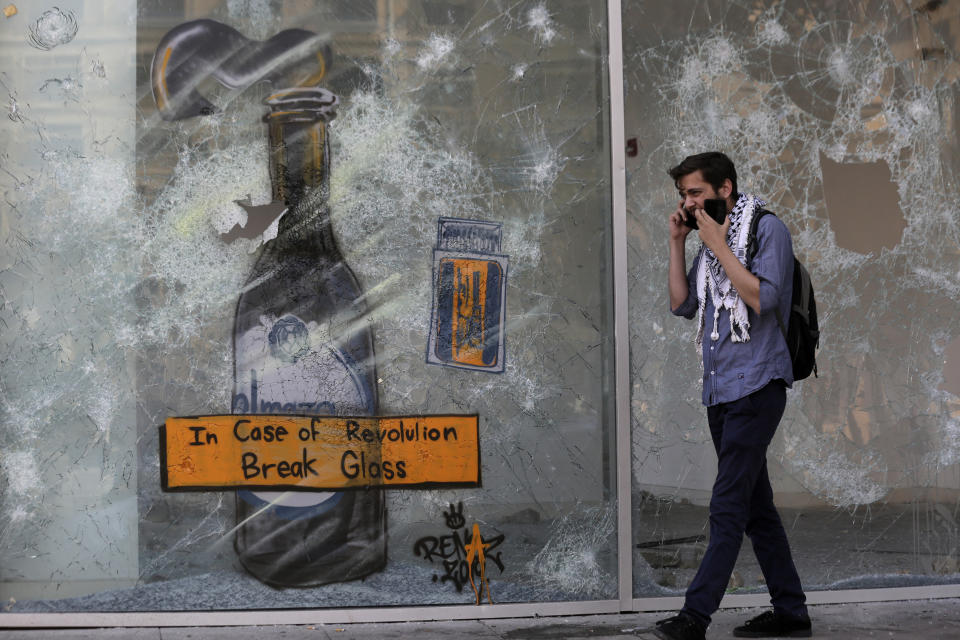 An anti-government protester speaks on a mobile phone as walks in front of a shop that damaged by protesters in the aftermath of a protest against the Lebanese government in Beirut, Lebanon, Monday, Oct. 21, 2019. Protesters have closed major roads around Lebanon ahead of an emergency Cabinet meeting to discuss a rescue plan for the country's crumbling economy. AP Photo/Hassan Ammar)