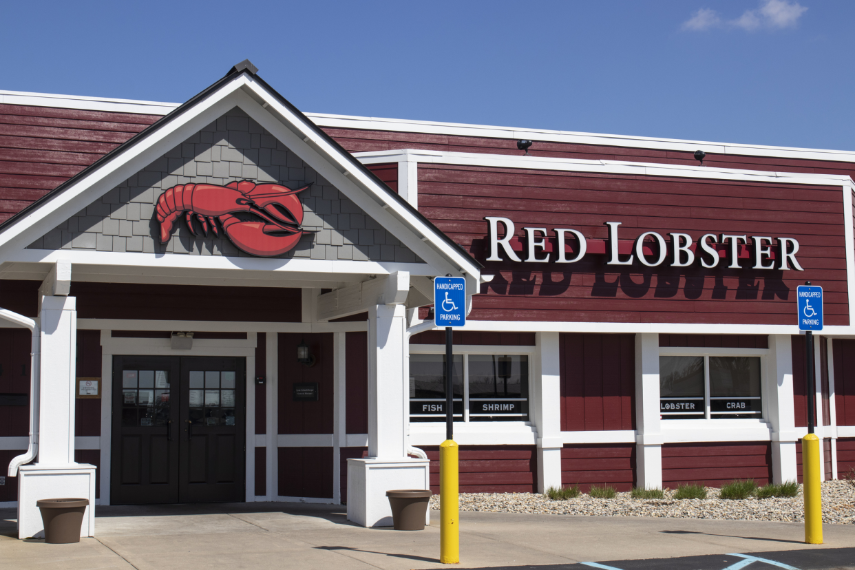 Front exterior of a Red Lobster restaurant in Indianapolis, Indiana with front doors, windows, and two handicapped parking spots, against a blue sky