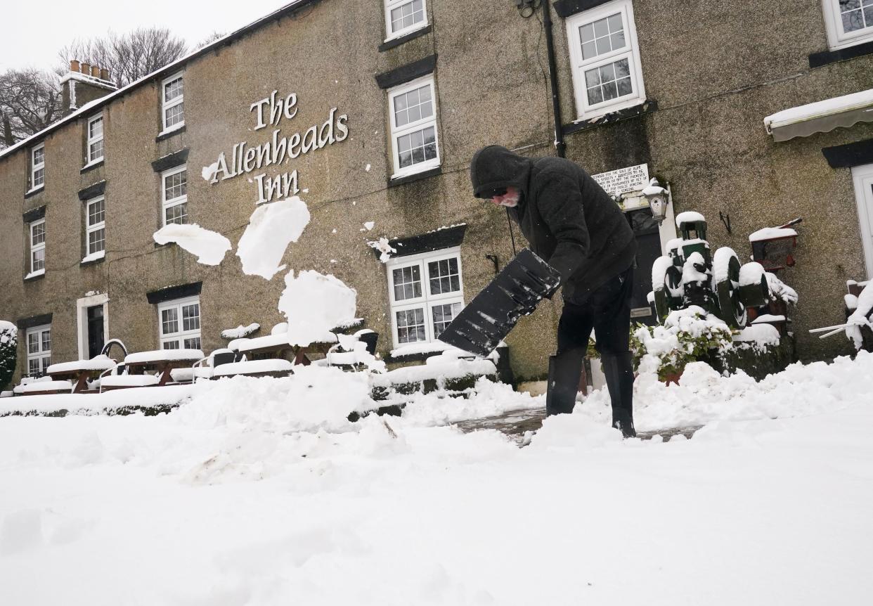 A person clears snow outside The Allenheads Inn in Allenheads, Northumberland (PA)