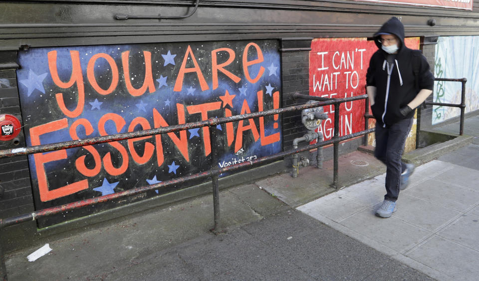 FILE - In this Thursday, April 16, 2020 file photo, a pedestrian walks past artwork painted on plywood covering a business closed during the coronavirus outbreak in Seattle. (AP Photo/Elaine Thompson)