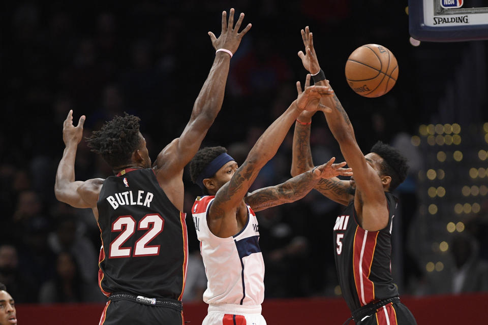 Washington Wizards guard Bradley Beal, center, passes the ball between Miami Heat forward Jimmy Butler (22) and forward Derrick Jones Jr. (5) during the first half of an NBA basketball game, Sunday, March 8, 2020, in Washington. (AP Photo/Nick Wass)