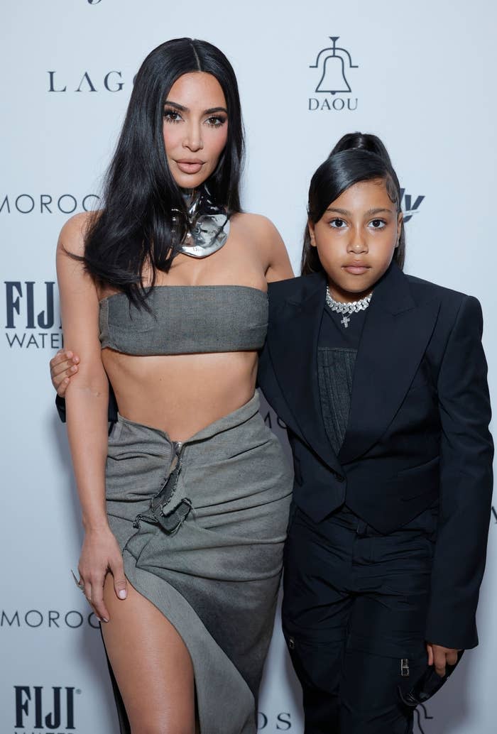 Kim Kardashian and North West on the red carpet. Kim is in a crop top, and a skirt with a metallic choker. North is in a suit and a pearl necklace