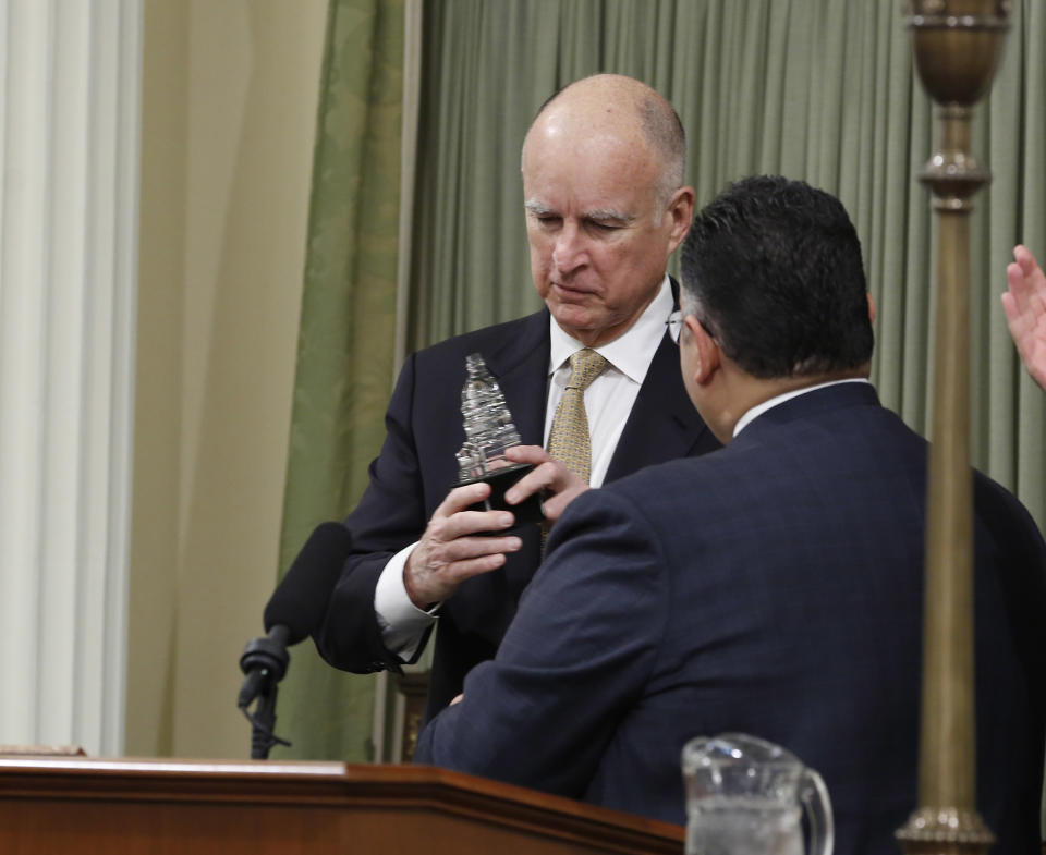 Gov. Jerry Brown, left, looks at the remembrance he was given, by Assembly Speaker John Perez, D-Los Angeles, right, for delivering the most State of the State addresses than any other governor in California history, during a joint session of the Legislature at the Capitol in Sacramento, Calif., Wednesday, Jan. 22, 2014. Brown delivered a dual message in his annual address to lawmakers, that a California resurgence is well underway but is threatened by economic and environmental uncertainties.(AP Photo/Rich Pedroncelli)