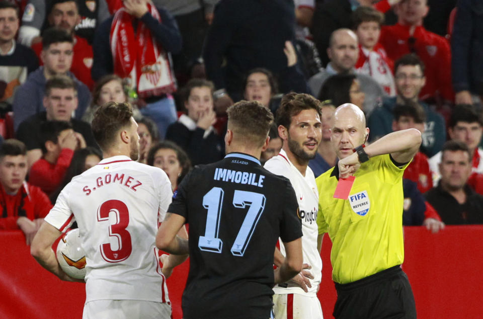 Referee Anthony Taylor, right, shows a red card to Sevilla's Franco Vazquez, second right, during the Europa League round of 32 second leg soccer match between Sevilla and Lazio at the Sanchez Pizjuan stadium, in Seville, Spain, Wednesday, Feb. 20, 2019. (AP Photo/Miguel Morenatti)