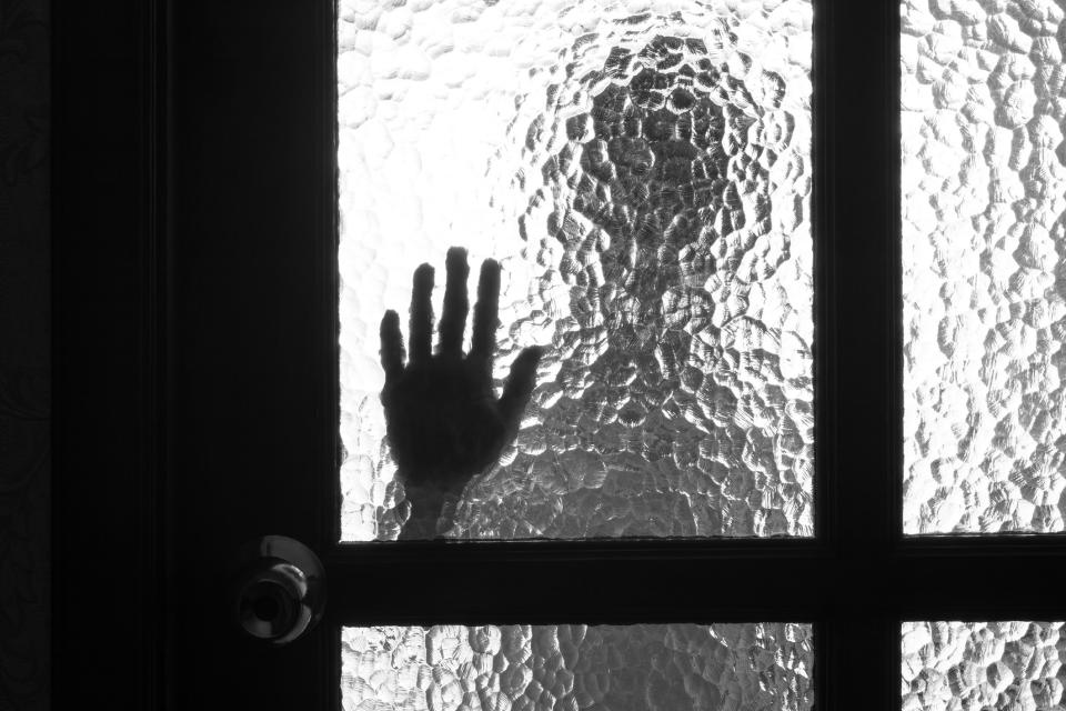 A hand is seen through a textured door