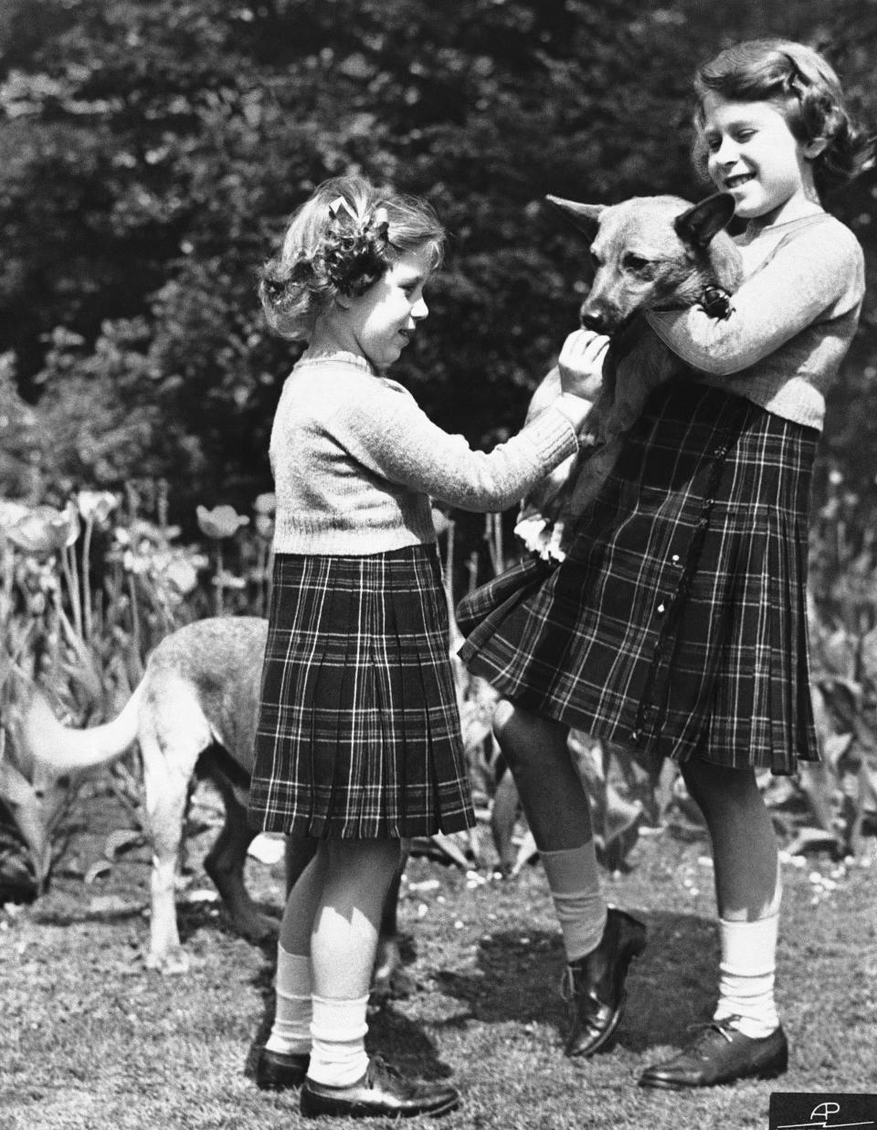 FILE - In this July 5, 1936 file photo, Britain's Princess Elizabeth, right, holds a Pembrokeshire Corgi as her sister Princess Margaret feeds it a biscuit. Queen Elizabeth II, Britain’s longest-reigning monarch and a rock of stability across much of a turbulent century, has died. She was 96. Buckingham Palace made the announcement in a statement on Thursday Sept. 8, 2022. (AP Photo, File)