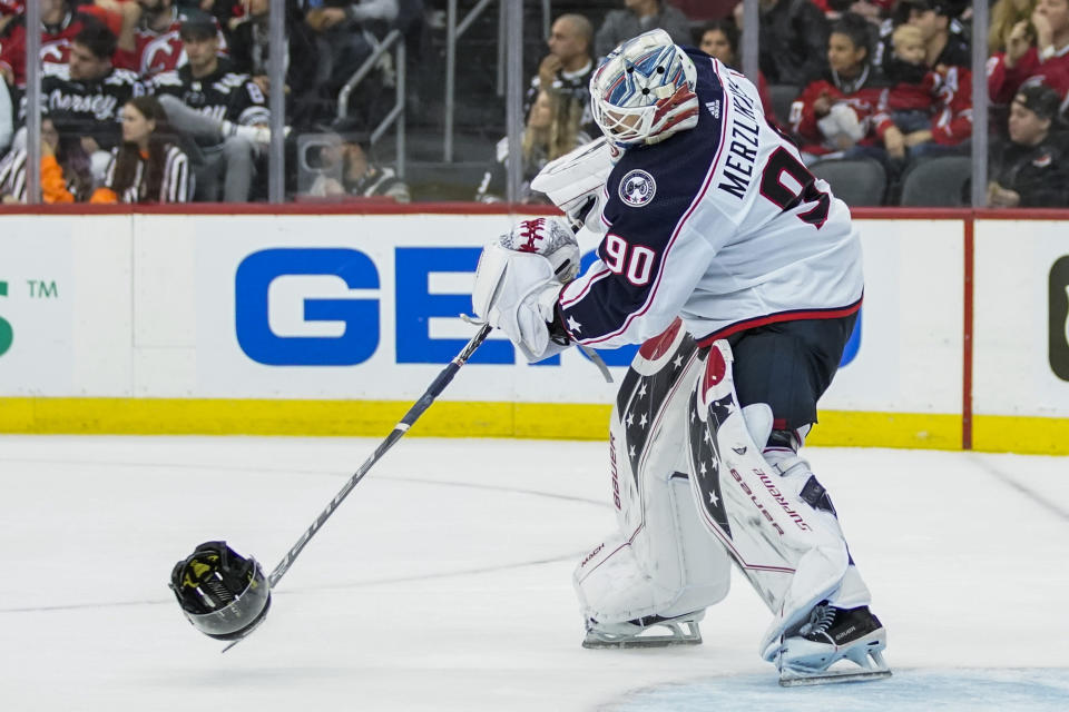 Columbus Blue Jackets goaltender Elvis Merzlikins (90) returns the helmet of New Jersey Devils left wing Miles Wood (44) after Wood was hit by a stick during the third period of an NHL hockey game Sunday, Oct. 30, 2022, in Newark, N.J. (AP Photo/Eduardo Munoz Alvarez)