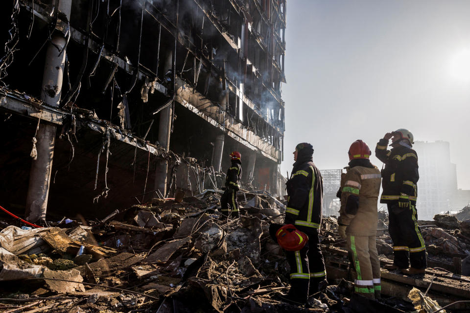 Rescue workers stand at the site of a bombing at a shopping center in Kyiv on March 21, 2022. (Thomas Peter / Reuters)