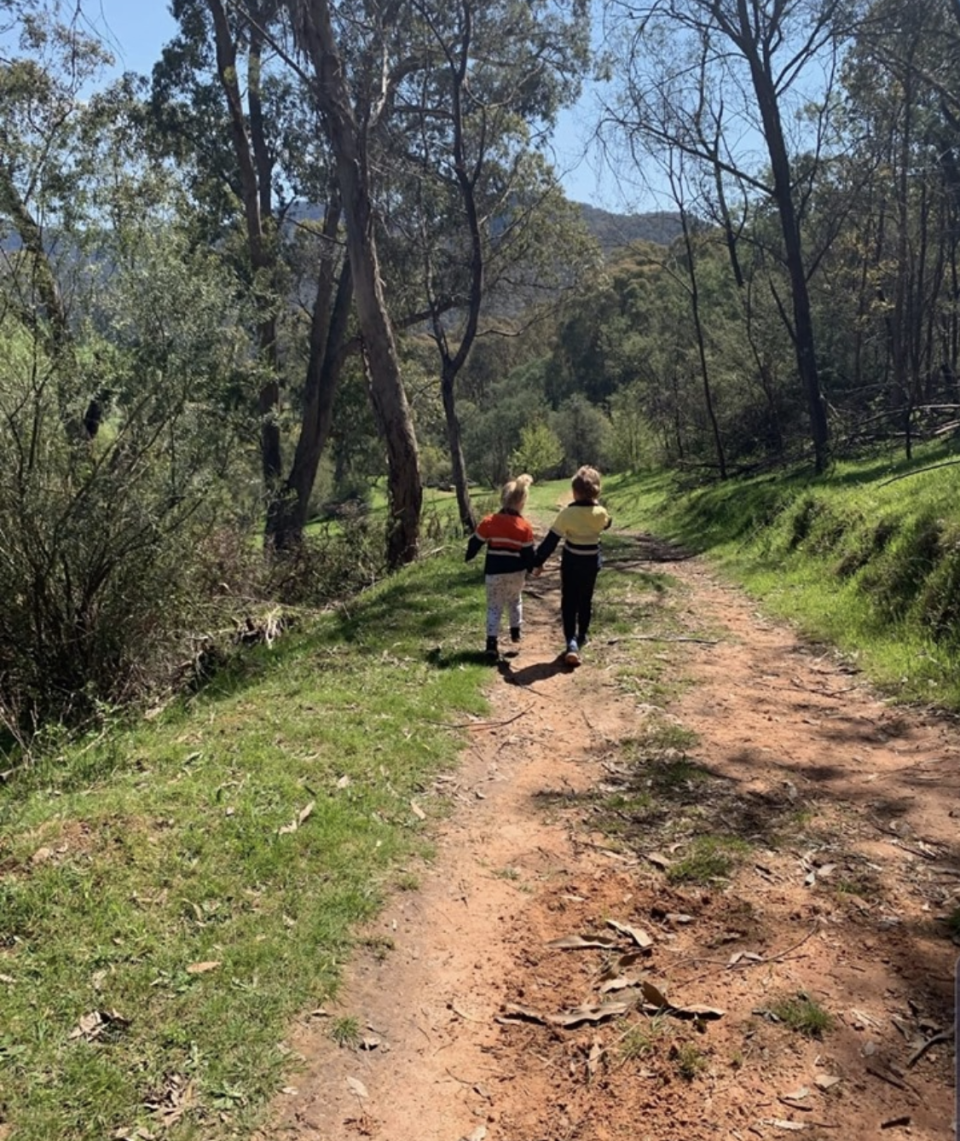 Two children hold hands and skip down a dirt path in Victoria with an eastern brown snake near their feet.