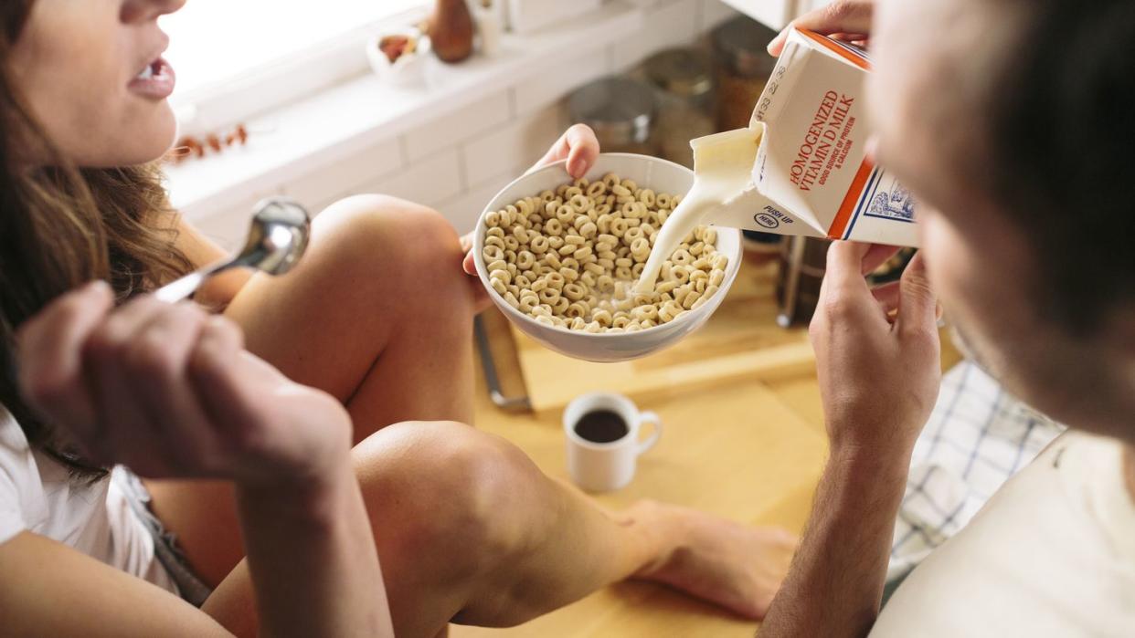 man pouring milk in bowl with breakfast cereal held by woman