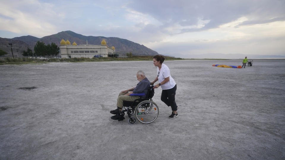 Robert Atkinson, 91, is pushed by his daughter Laurie Conklin along the receding shoreline before his flight over the Great Salt Lake on June 18, 2021, near Salt Lake City. A resort long since closed once drew sunbathers who would float like corks in the extra salty waters. Picnic tables once a quick stroll from the shore are now a 10-minute walk away. Atkinson remembers that resort and the feeling of weightlessness in the water. When he returned this year to fly over the lake in a motorized paraglider, he found it changed. "It's much shallower than I would have expected it to be," he said. (AP Photo/Rick Bowmer)