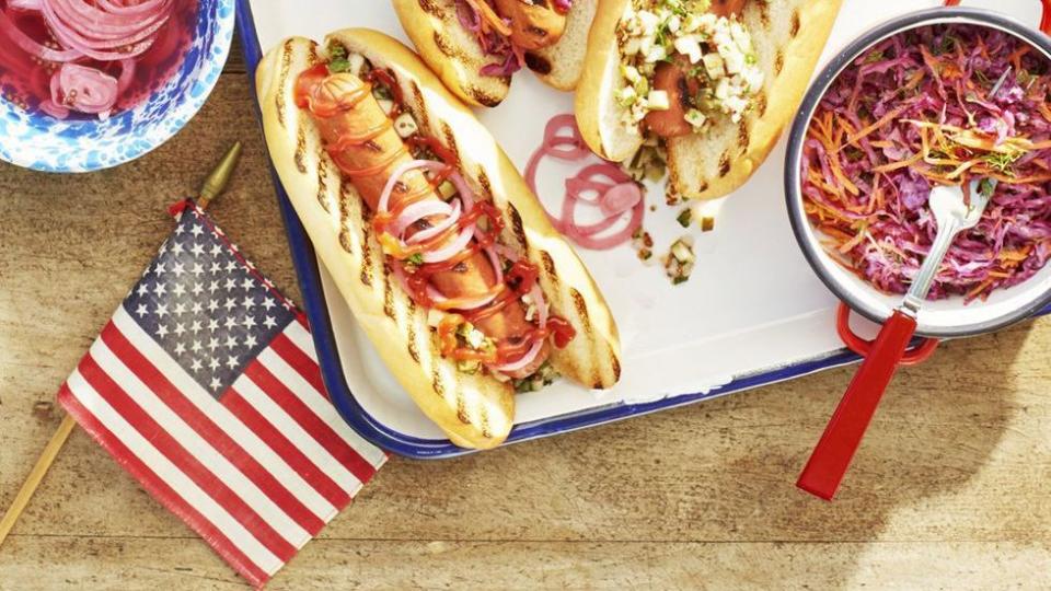 grilled hotdogs with various toppings on a white tray with blue trim