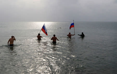 People hold Russian national flags as they take a dip in cold waters of the Black Sea during Orthodox Epiphany celebrations in the port city of Yevpatoriya, Crimea, January 19, 2016. REUTERS/Pavel Rebrov/File Photo
