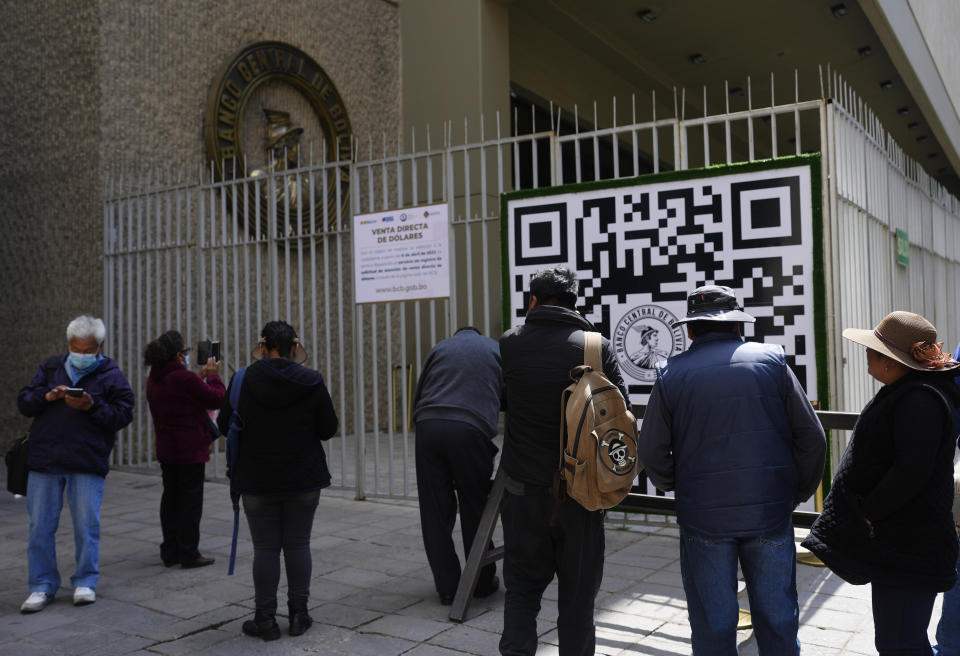 People look at a QR code outside the Central Bank of Bolivia that people must use to register to make an appointment with the bank which then tells the user how many U.S. dollars they can buy on that date, in La Paz, Bolivia, Tuesday, April 11, 2023. (AP Photo/Juan Karita)