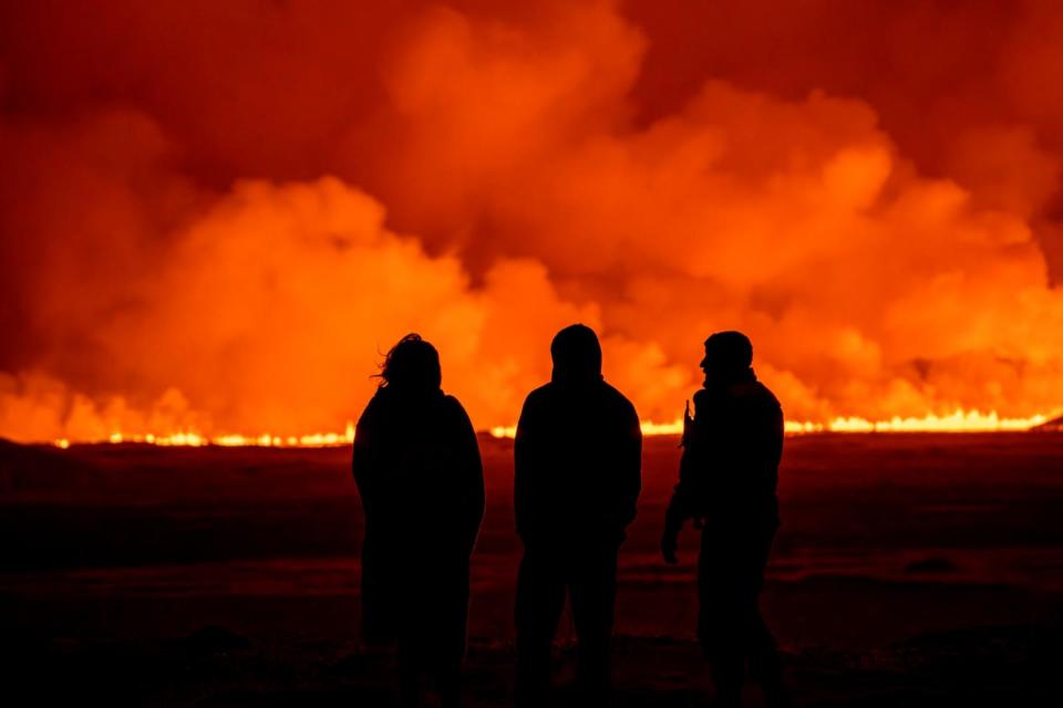PHOTO: People watch as the night sky is illuminated caused by the eruption of a volcano in Grindavik on Iceland's Reykjanes Peninsula, Monday, Dec. 18, 2023.  (Marco Di Marco/AP)
