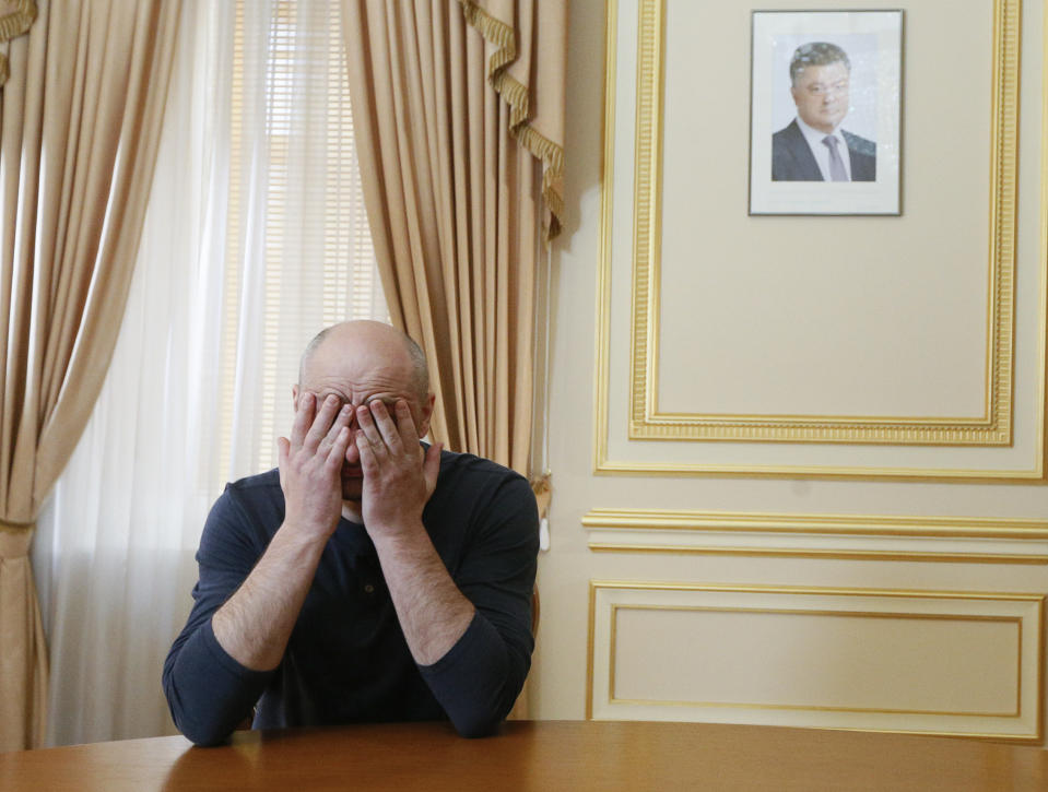 FILE - In this Thursday, May 31, 2018 file photo Russian journalist Arkady Babchenko holds his face during an interview with foreign media, with the portrait of Ukrainian President Petro Poroshenko, right in the background, in Kiev, Ukraine. Arkady Babchenko detailed the deception to reporters Thursday for the first time since Ukrainian authorities revealed they had staged his death to foil an alleged plot on his life by Moscow's security services. (Valentyn Ogirenko/Pool Photo via AP, File)