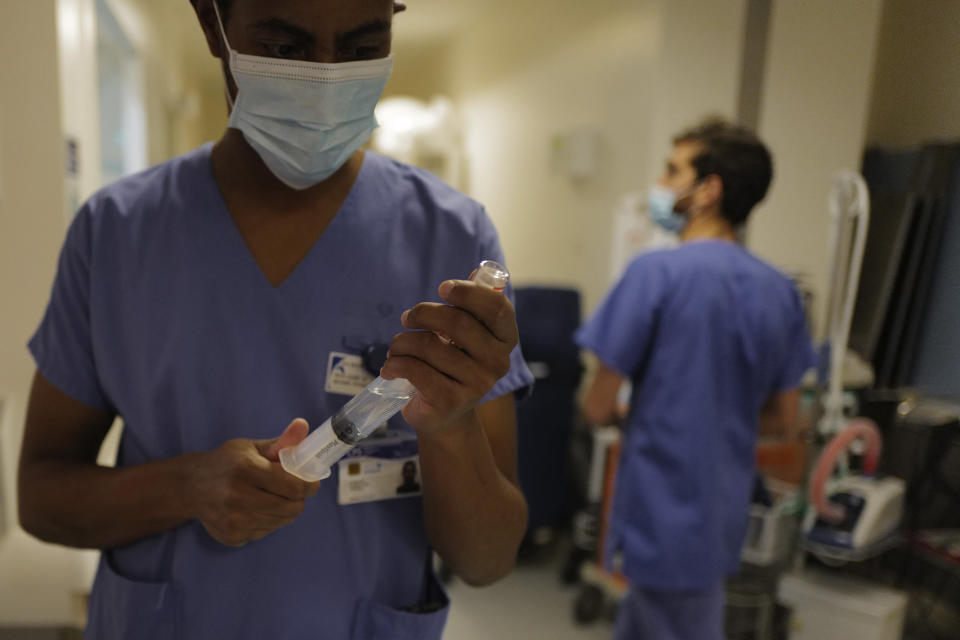 Nurse Hyad Boina, left, prepares a syringe to use in the treatment of a patient in room No. 9 in his battle against COVID-19 at Bichat Hospital, AP-HP, in Paris Tuesday, Dec. 1, 2020. (AP Photo/Francois Mori)