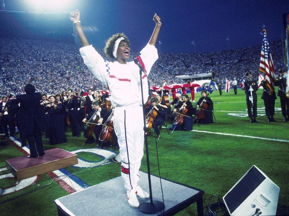 Whitney Houston sings the National Anthem during the pregame show at Super Bowl XXV while tens of thousands of football fans wave tiny American flags in an incredible outburst of patriotism during the Persian Gulf War on 01/27/1991