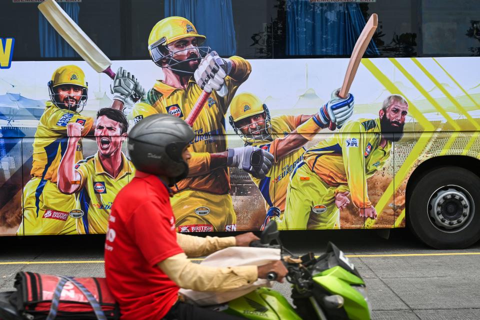 A food delivery worker drives past the bus of Indian Premier League's (IPL) Chennai Super Kings in Mumbai on March 24, 2022. (Photo by Indranil MUKHERJEE / AFP) (Photo by INDRANIL MUKHERJEE/AFP via Getty Images)