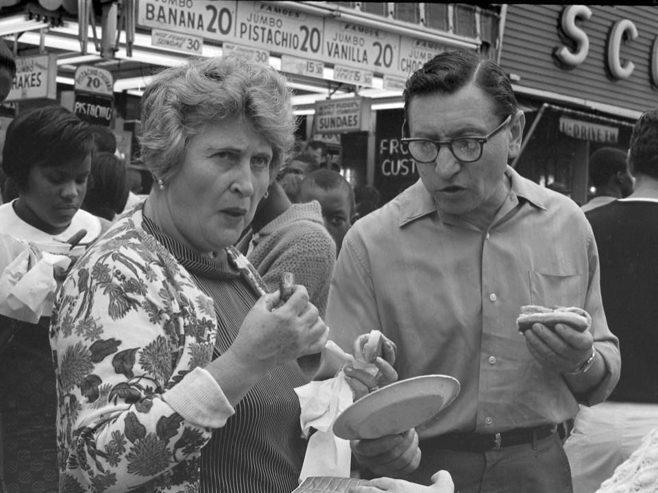 A couple eat hot dogs in front of Nathan's Famous fast food restaurant at Coney Island on July 4, 1968