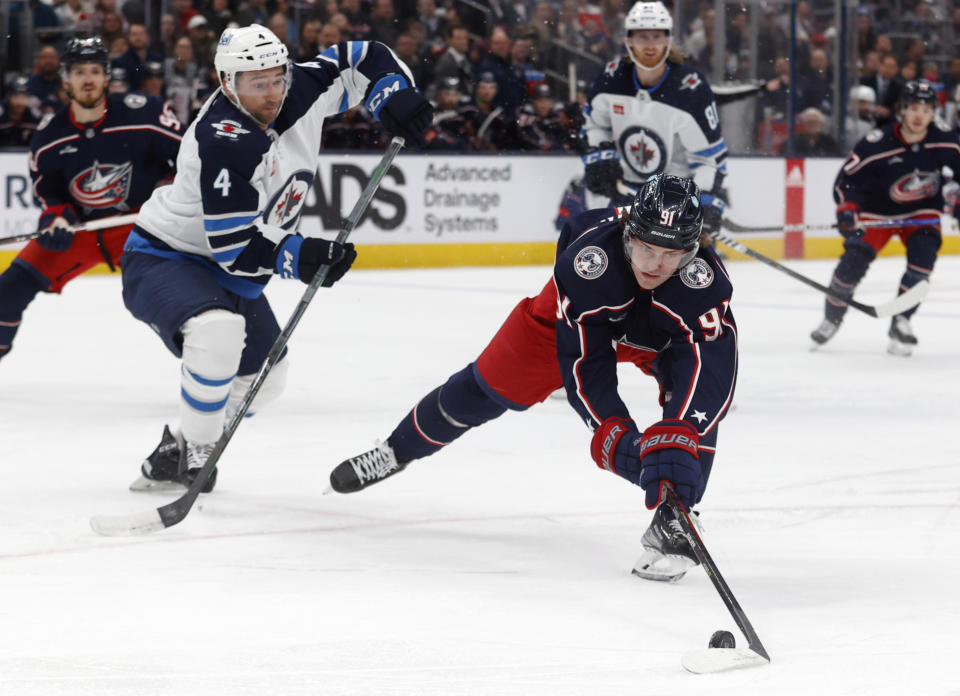 Columbus Blue Jackets forward Kent Johnson, right, reaches for the puck in front of Winnipeg Jets defenseman Neal Pionk (4) during the second period of an NHL hockey game in Columbus, Ohio, Thursday, Feb. 16, 2023. (AP Photo/Paul Vernon)