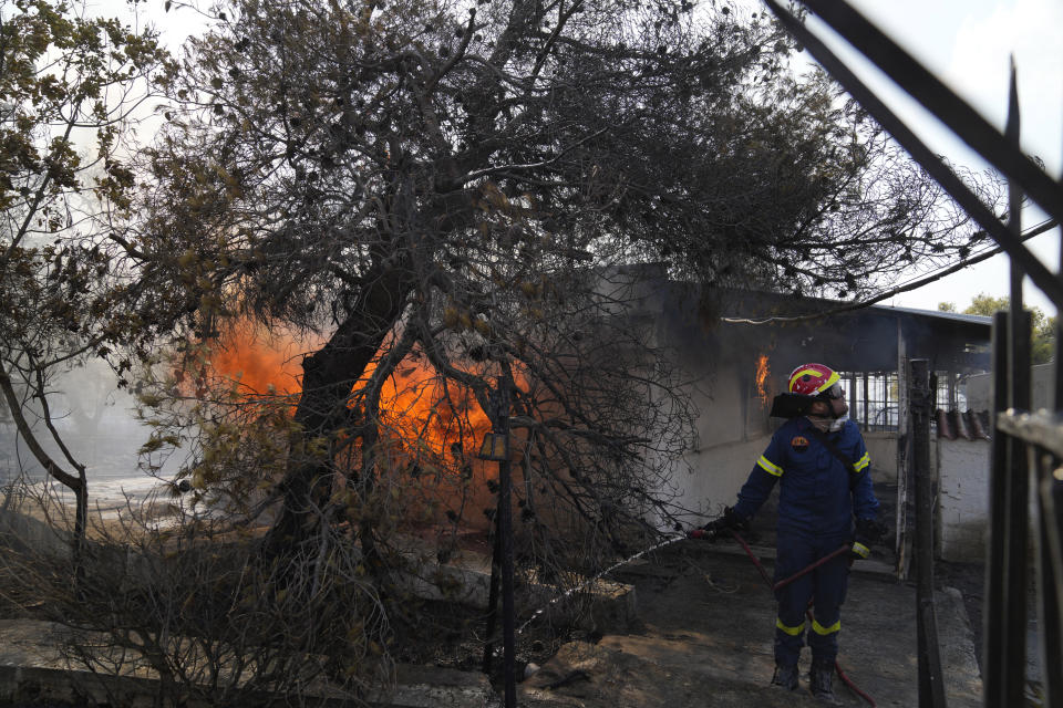A firefighter extinguish the fire to a house during a wildfire in Thea area some 60 kilometers (37 miles) northwest of Athens, Greece, Thursday, Aug. 19, 2021. A major wildfire northwest of the Greek capital devoured large tracts of pine forest for a third day and threatened a large village as hundreds of firefighters, assisted by water-dropping planes and helicopters, battled the flames Wednesday. (AP Photo/Thanassis Stavrakis)