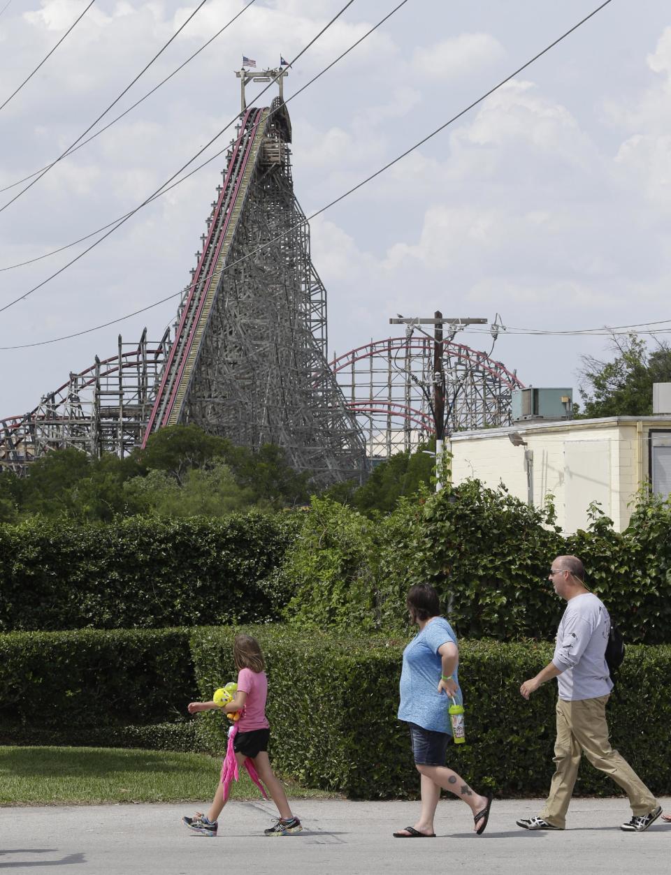 The Texas Giant roller coaster ride sits idle as people walk nearby looking from outside the Six Flags Over Texas park Saturday, July 20, 2013, in Arlington, Texas. Investigators will try to determine if a woman who died while riding the roller coaster at the amusement park Friday night fell from the ride after some witnesses said she wasn't properly secured.(AP Photo/LM Otero )