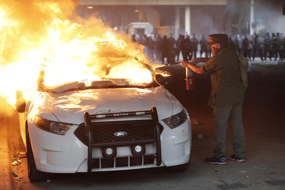 A man tries to use a fire extinguisher on a buring police car during a demonstration next to the city of Miami Police Department, Saturday, May 30, 2020, downtown in Miami. Protests were held throughout the country over the death of George Floyd, a black man who died after being restrained by Minneapolis police officers on May 25. (AP Photo/Wilfredo Lee)