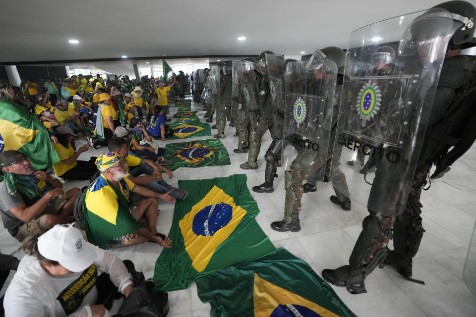 FILE - Supporters of Brazil's former President Jair Bolsonaro sit in front of a line of military police inside the Planalto presidential palace after storming the official workplace of the president, in Brasilia, Brazil, Jan. 8, 2023. A year later, around 400 people remain jailed facing charges for the riots and Bolsonaro has been under investigation by the Supreme Court about his role in the mayhem. (AP Photo/Eraldo Peres, File)