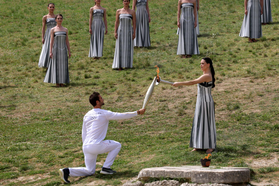 The first torchbearer, 2020 Olympic rowing champion Stefanos Ntouskos, receives the flame from Greek actress Mary Mina, who plays the high priestess, during the lighting ceremony for Paris 2024 on the site of Ancient Olympia.  / Credit: Socrates Baltagiannis/picture alliance via Getty Images