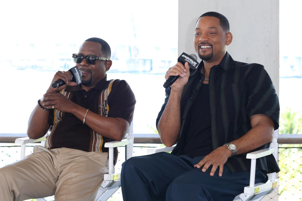 Martin Lawrence and Will Smith sit on director's chairs, holding microphones and smiling during an interview