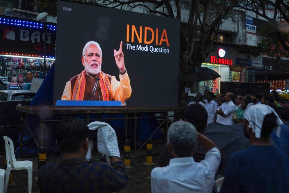 People watch an outdoor screen with title: India, the Modi question
