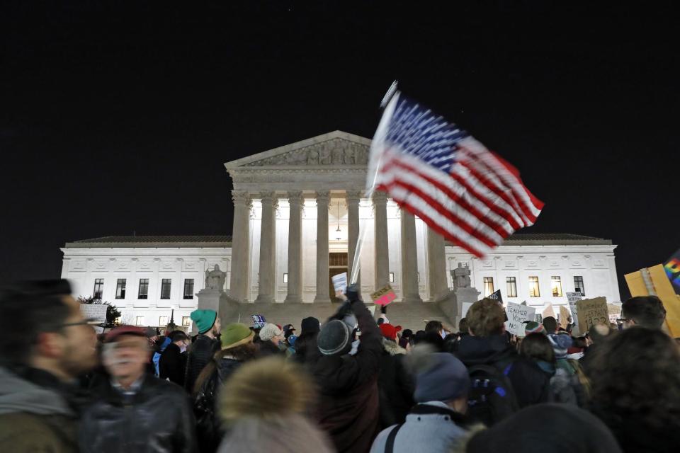 In this Jan. 30, 2017, photo, a protester waves an American flag in front of the Supreme Court during a protest about President Donald Trump's recent executive orders in Washington. Two weeks into his presidency, Donald Trump has thrown Washington into a state of anxious uncertainty. Policy pronouncements sprout up from the White House in rapid succession. Some have far-reaching implications, most notably Trump’s temporary refugee and immigration ban, but others disappear without explanation, including planned executive actions on cybersecurity and the president’s demand for an investigation into unsubstantiated voter fraud. The day’s agenda can quickly be overtaken by presidential tweets, which often start flashing on smartphones just as the nation’s capital is waking up. (AP Photo/Alex Brandon)