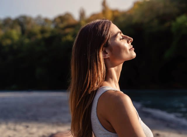 woman with closed eyes basks in the sun while meditating outdoors on a beach