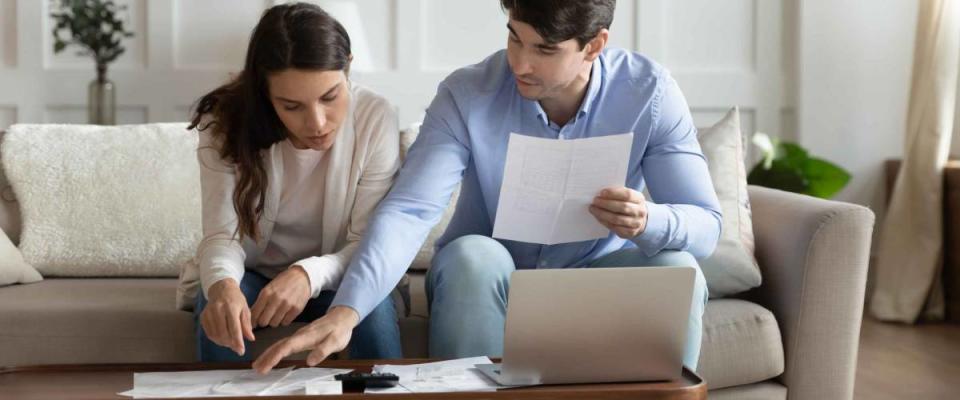 Concentrated attentive millennial spouses sitting on couch at home discussing whether to refinance their mortgage.