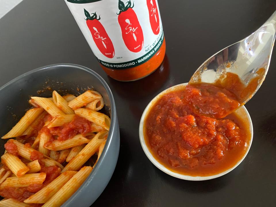 spoon showing close-up of smt tomato sauce with a bowl of pasta in the background