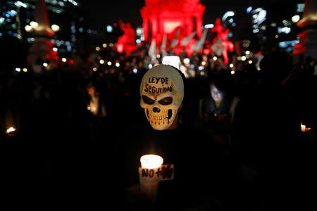 An activist in mask holds a candle during a protest against a new security bill, Law of Internal Security, in Mexico City, Mexico, December 13, 2017. The words on the mask read, "Law of security". REUTERS/Edgard Garrido